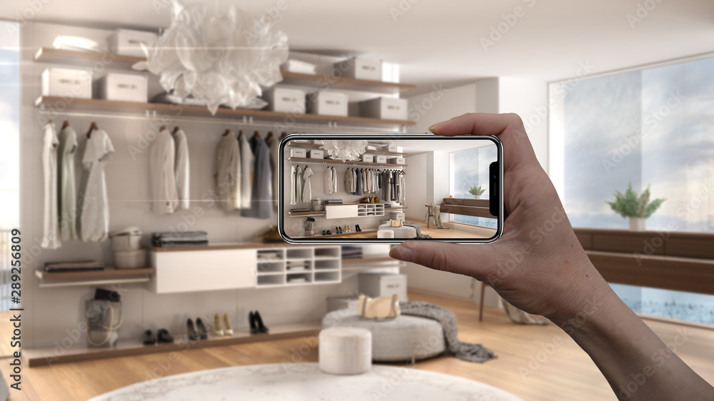 Hand holding smart phone, AR application, simulate furniture and interior design products in real home, architect designer concept, blur background, modern bedroom with walk-in closet Hand holding smart phone, AR application, simulate furniture and interior design products in real home, architect designer concept, blur background, modern bedroom with walk-in closet