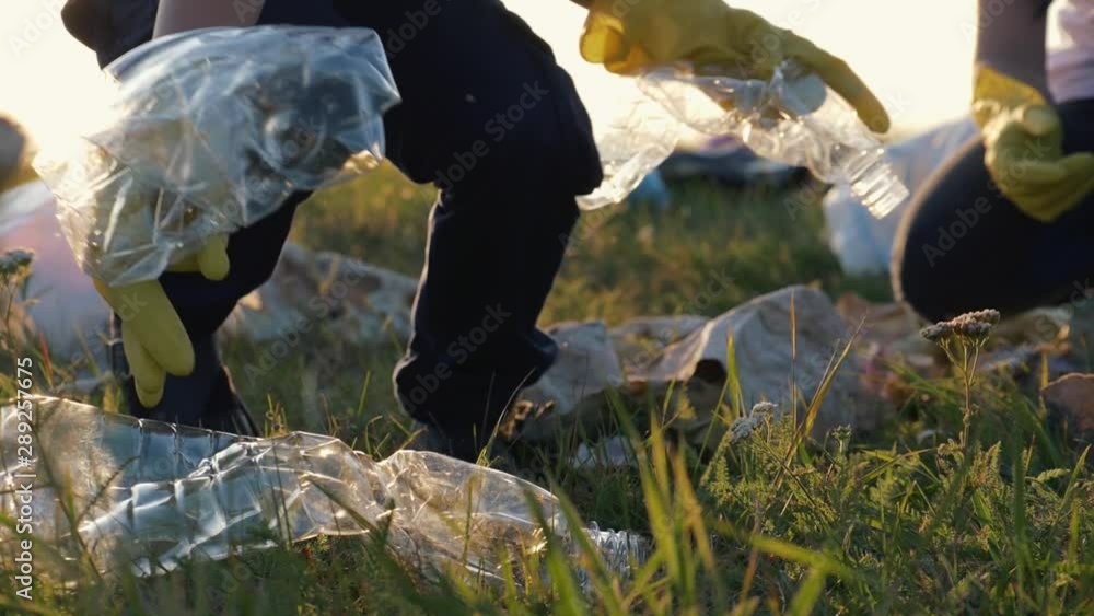 Teamwork. A happy family helps to keep nature clean and collects trash from the green field at sunset. The concept of garbage collection. Volunteers save the world from environmental disaster. Teamwork. A happy family helps to keep nature clean and collects trash from the green field at sunset. The concept of garbage collection. Volunteers save the world from environmental disaster.