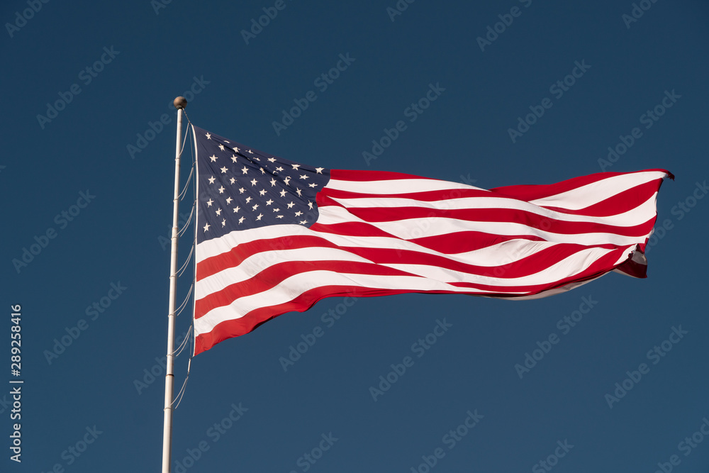 Flag of the USA is waving on blue sky background. National symbol of the United States of America, independence, patriotism, freedom, honor, democracy concept