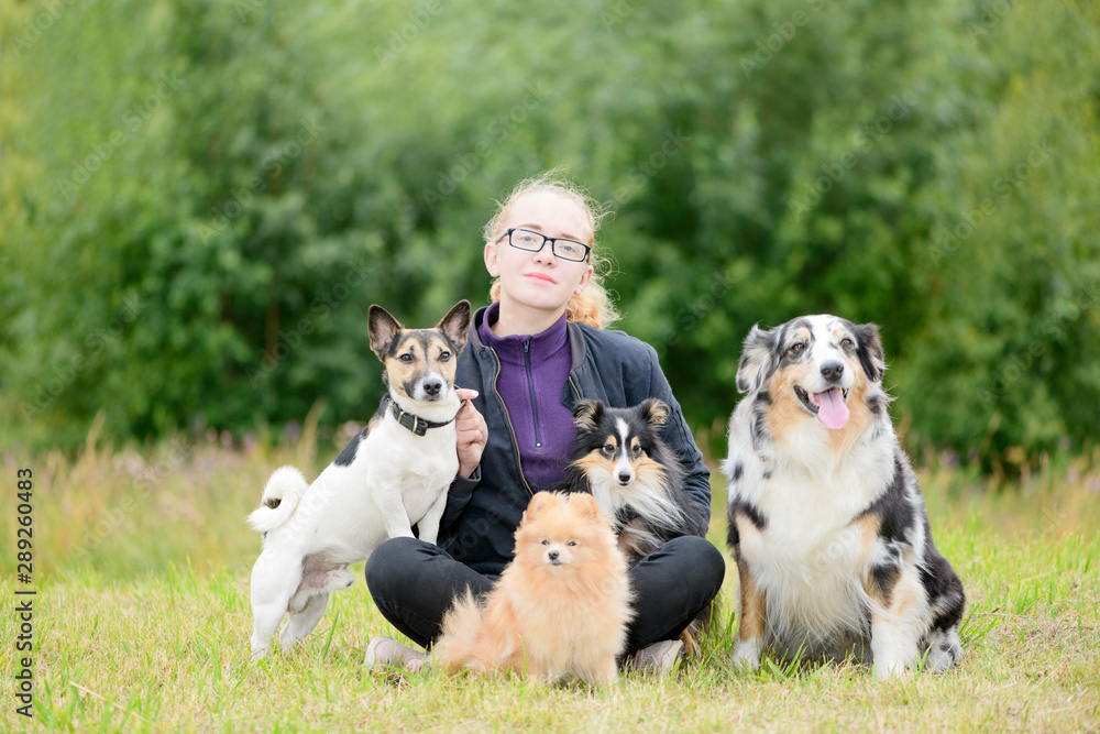 The blonde teenage girl, 16 years old, with the glasses and her dogs are sitting on the grass in a park.