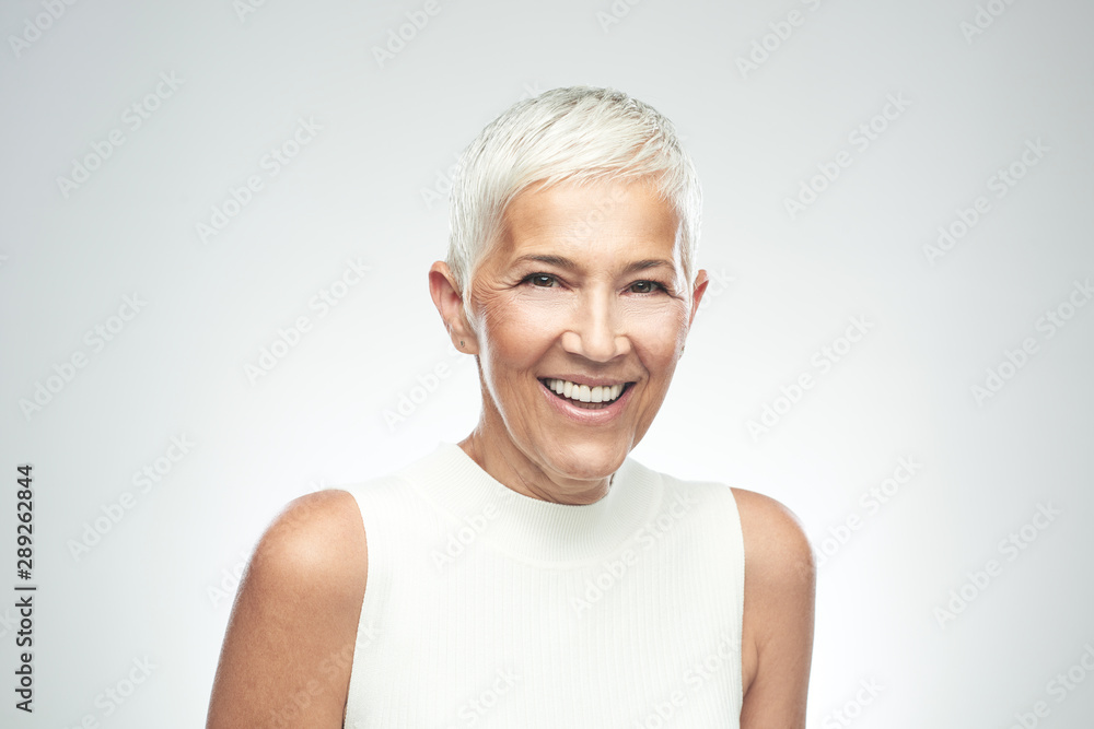 Beautiful smiling senior woman with short gray hair posing in front of gray background. Beauty photography. Beautiful smiling senior woman with short gray hair posing in front of gray background. Beauty photography.