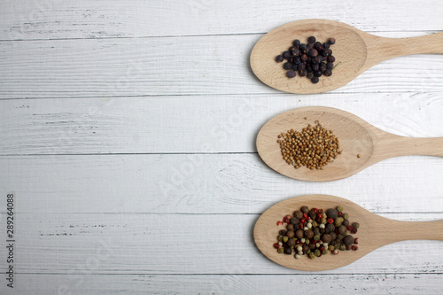 juniper, cumin and peppercorn mix in serving spoons on wooden background. Image contains copy space