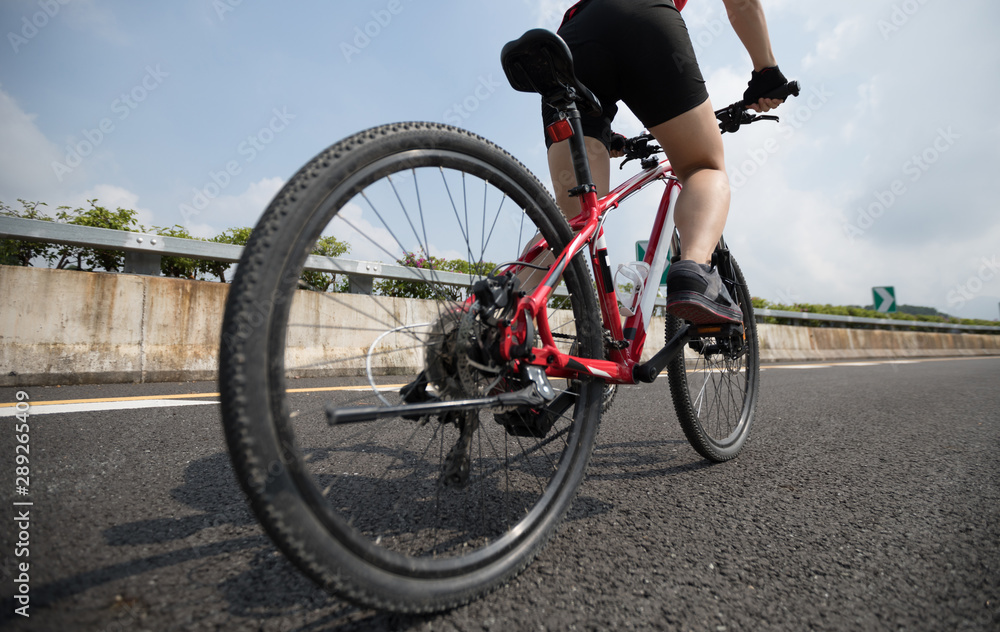 Woman cyclist legs riding Mountain Bike on highway Woman cyclist legs riding Mountain Bike on highway