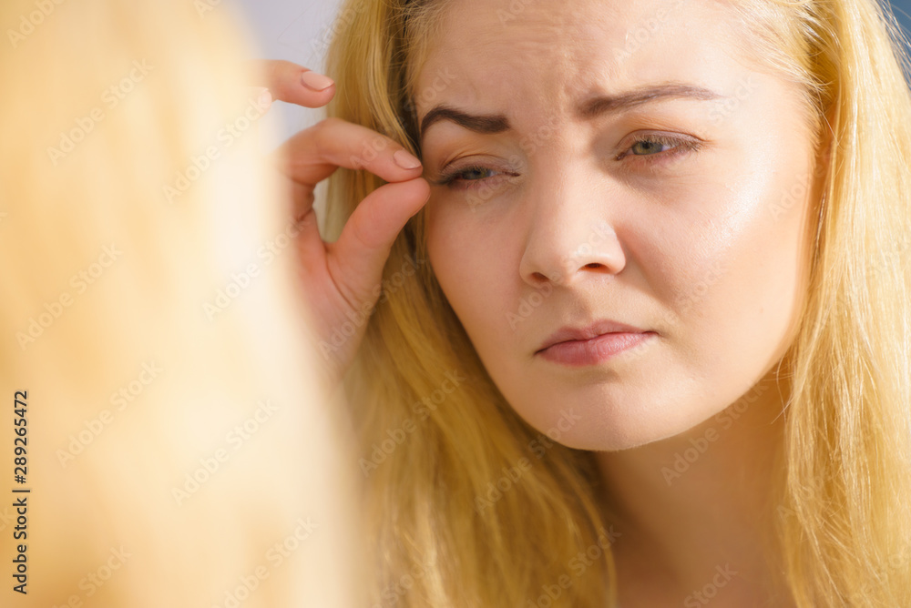 Naklejka premium Woman looking at her skin in mirror