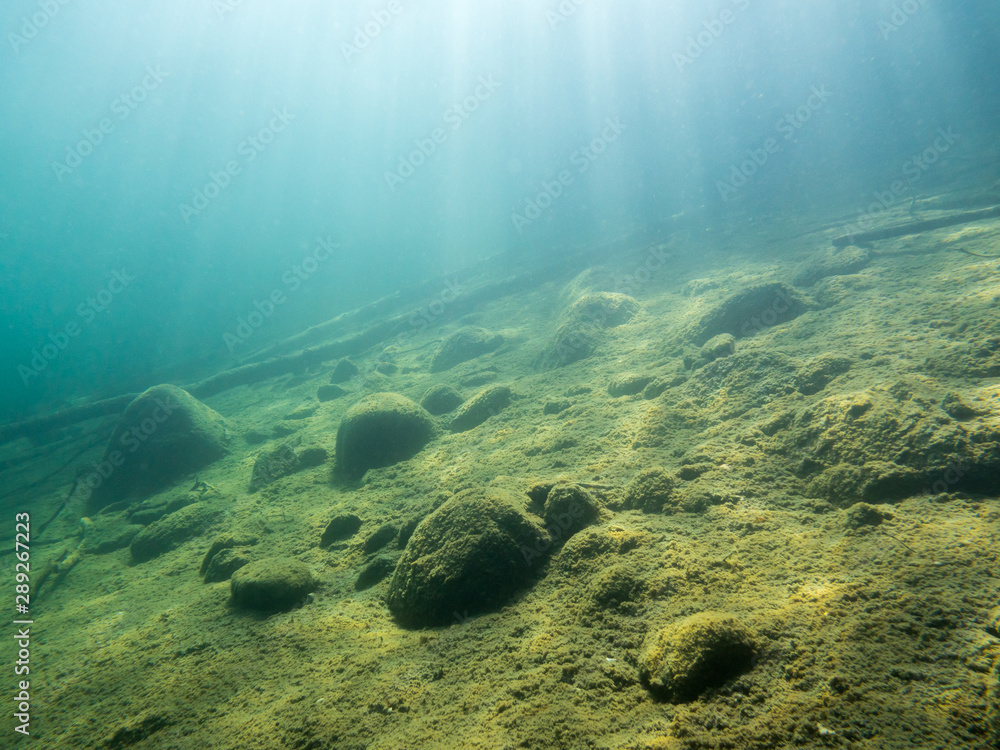 Fototapeta premium Underwater view of sloping bottom with sunrays at clear-watered lake.