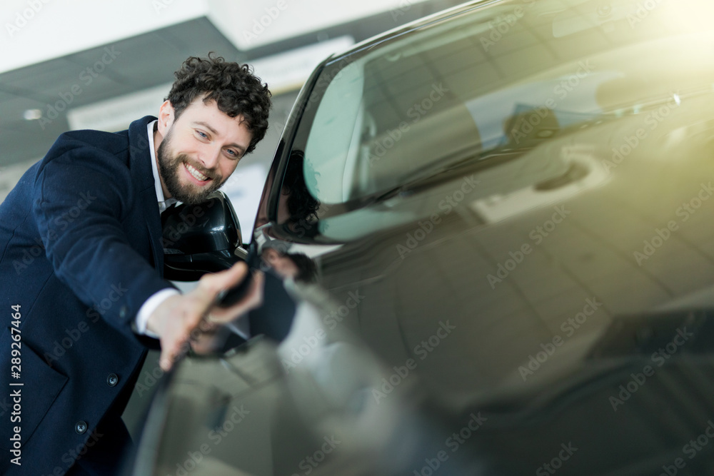 Handsome young man in classic blue suit is smiling while examining car in a motor show Handsome young man in classic blue suit is smiling while examining car in a motor show