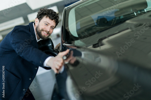 Handsome young man in classic blue suit is smiling while examining car in a motor show