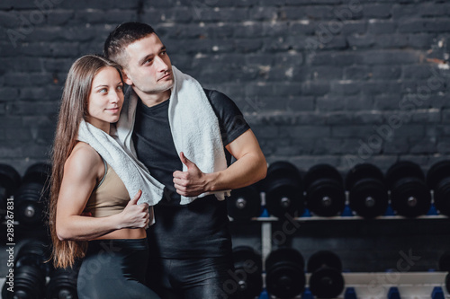 Young sporty couple guy and girl standing in gym. During this, the white scumbag is held on the neck. Standing on a black background and looking away. photo