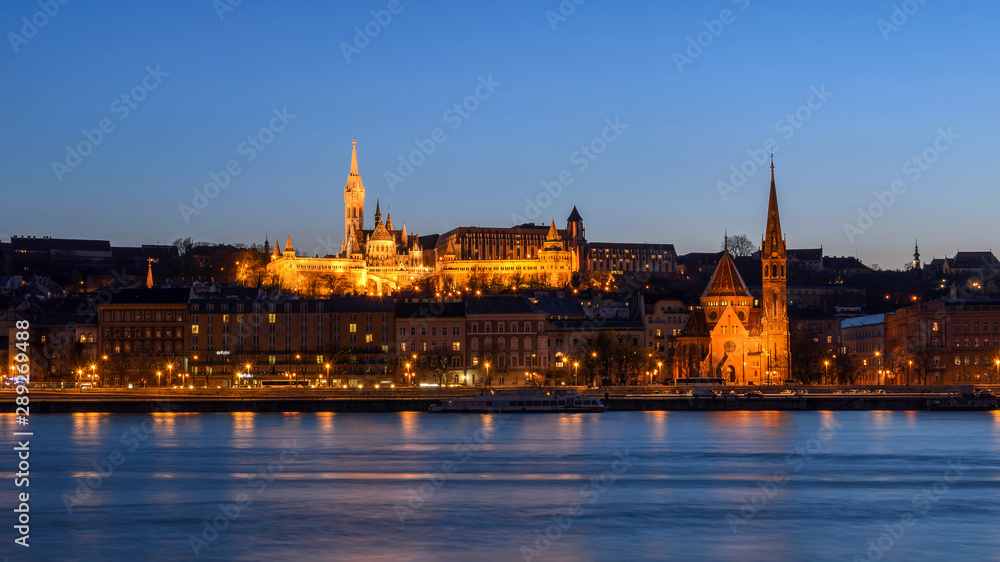 Panoramic view of Szilágyi Dezső Square Reformed Church and Matthias Church on the west bank of the river Danube captured at the blue hour.