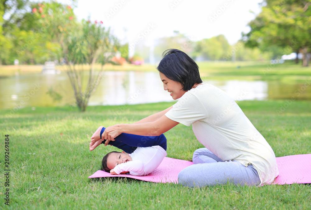 Fototapeta premium Portrait of Asian mother doing baby yoga for her son on green lawn in the nature garden outdoor.