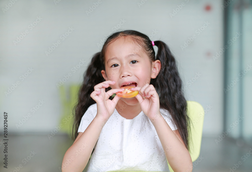Happy little Asian child girl eating a piece of sliced tomato. Kid eating healthy food concept. Happy little Asian child girl eating a piece of sliced tomato. Kid eating healthy food concept.