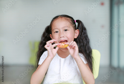Happy little Asian child girl eating a piece of sliced tomato. Kid eating healthy food concept.