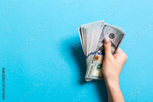 Top view of female hand holding a pack of one hundred dollar bills on colorful background. Wage and salary concept with empty space for your design