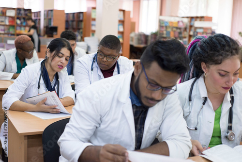 Multinational group of young students at a medical university studying medical journals while sitting at a table in a classroom