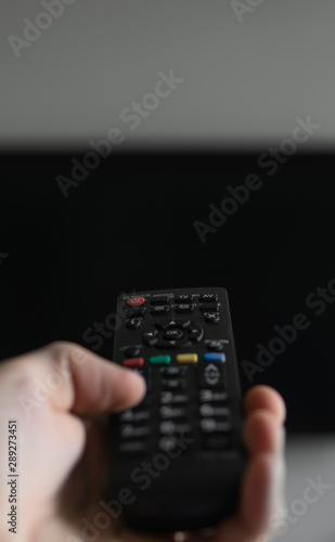 Quadro su tela The man with the remote control in hand want switch on the TV and presses the button on the remote control