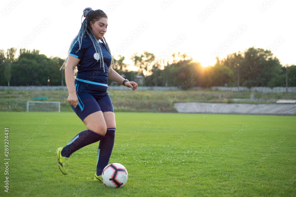 young woman kicks a soccer ball with her foot. Not sporty girl, on the green grass, football field