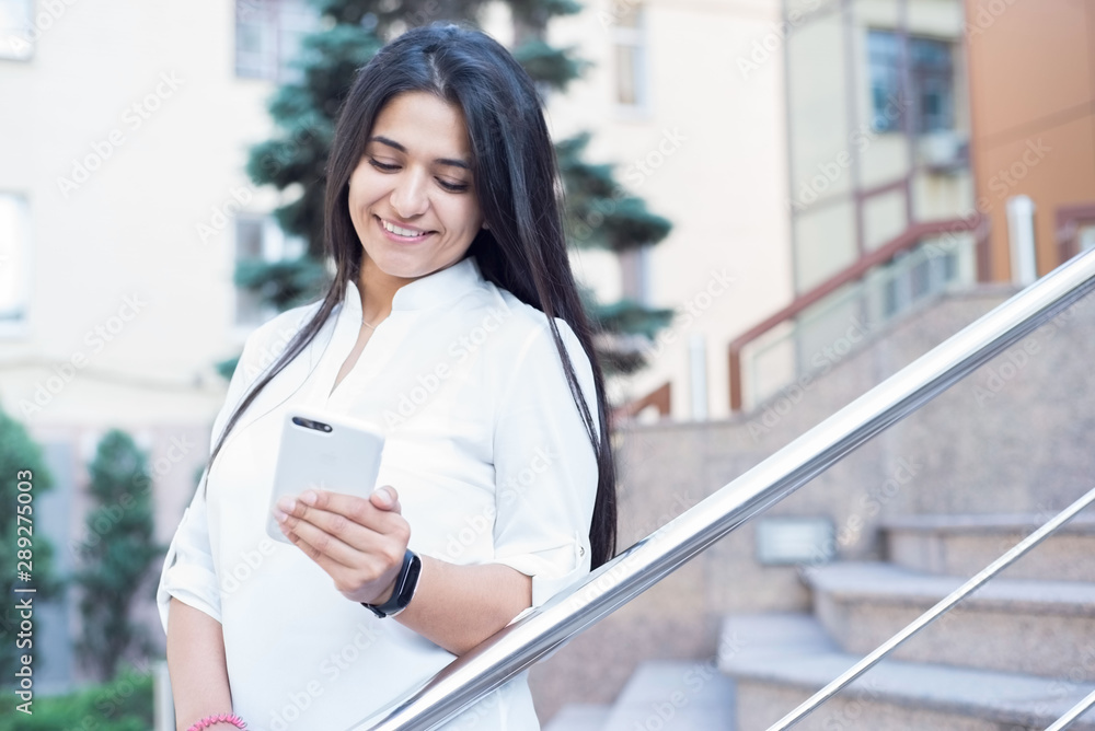 portrait of a beautiful indian girl. Business woman, student, smiling. Stands at the office building, uses a smartphone portrait of a beautiful indian girl. Business woman, student, smiling. Stands at the office building, uses a smartphone