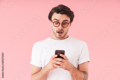 Image of unshaven shocked man wearing eyeglasses looking and typing at cellphone © Drobot Dean