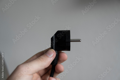 Hand holding black electric plug on a grey background.