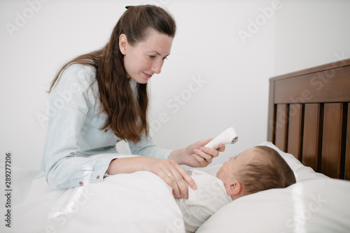 Woman measures temperature. The kid is sick lying in bed