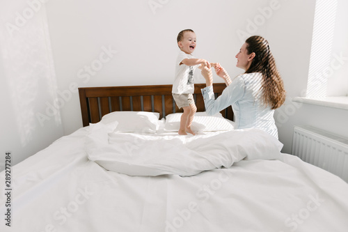 Mother and child having fun in bedroom/ They are jumping and hugging
