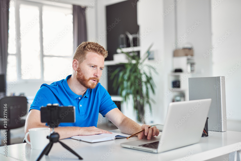 Handsome Caucasian ginger employee dressed casaul looking at laptop and working on big project while sitting in modern office.