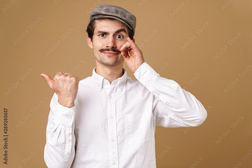 Image closeup of happy man wearing hat touching his mustache and pointing finger aside at copyspace Image closeup of happy man wearing hat touching his mustache and pointing finger aside at copyspace