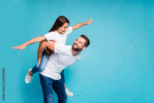 Profile side photo of cheerful people holding hands playing piggyback wearing white t-shirt denim jeans isolated over blue background photo