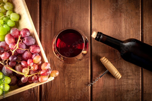 Cellar Tasting. A photo of a red wine glass with a bottle, grapes, and a vintage corkscew, shot from the top on a dark rustic wooden background
