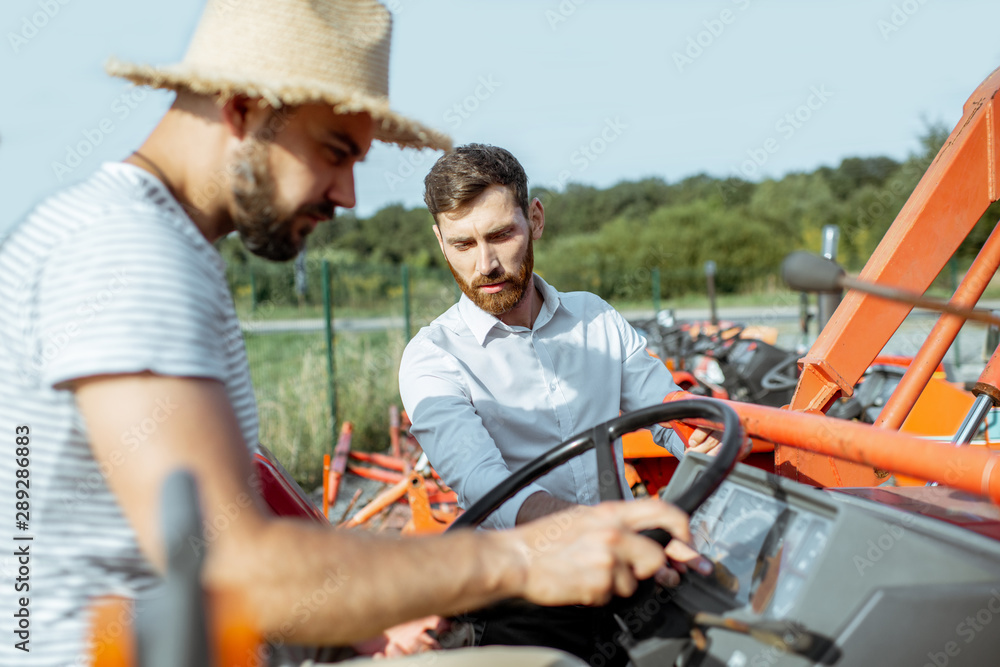 Young agronomist with elegant salesman choosing a tractor for farming on the open ground of agricultural shop