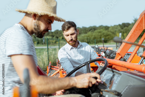Young agronomist with elegant salesman choosing a tractor for farming on the open ground of agricultural shop