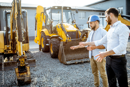 Builder choosing heavy machinery for construction with a sales consultant on the open ground of a shop with special vehicles photo