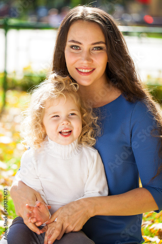 Closeup portrait of a young beautiful mother with little curly daughter in autumn park