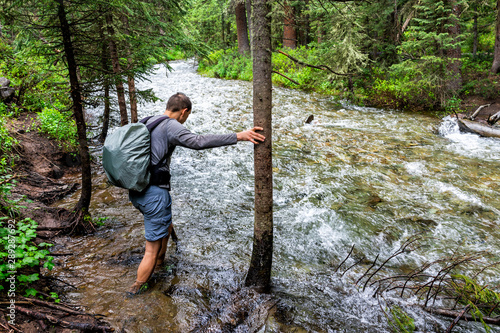 Man crossing river ford on Conundrum Creek Trail in Aspen, Colorado in 2019 summer in forest woods with strong current