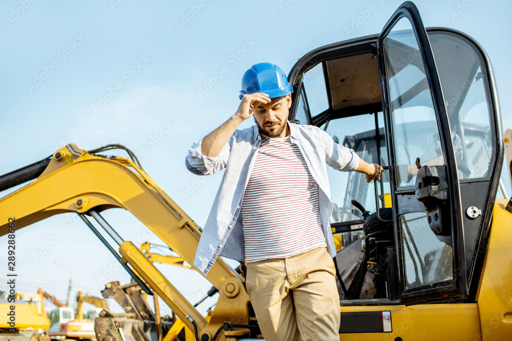 Handsome builder or construction worker getting out of the escavator on the construction site Handsome builder or construction worker getting out of the escavator on the construction site