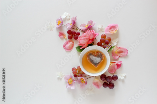 Pink floral arrangement with a cup of tea with a heart shape tea bag inside on a white background