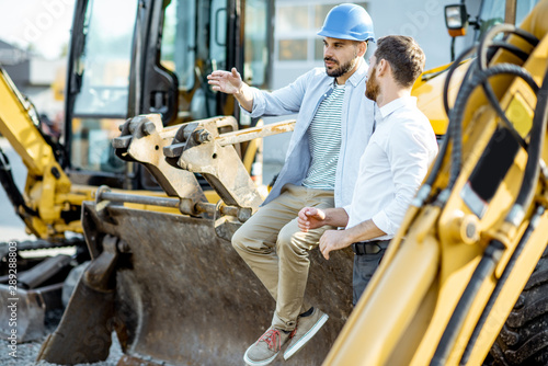 Builder choosing heavy machinery for construction, talking with a sales consultant on the open ground of a shop with special vehicles