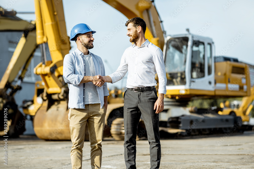 Builder choosing heavy machinery for construction, talking with a sales consultant on the open ground of a shop with special vehicles Builder choosing heavy machinery for construction, talking with a sales consultant on the open ground of a shop with special vehicles