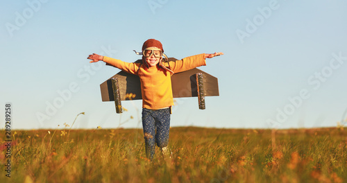 Fotografia Child pilot aviator with wings of airplane dreams of traveling in summer  at sun