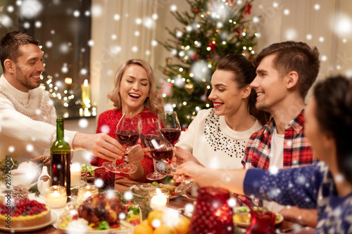 holidays and celebration concept - happy friends having christmas dinner at home, drinking red wine and clinking glasses over snow