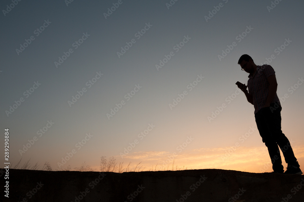 silhouette of man with cell phone at sunset