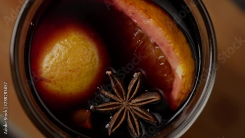 Top view of spinning glass mug with mulled wine. On top of vine surface anise star and slice of orange. Close up