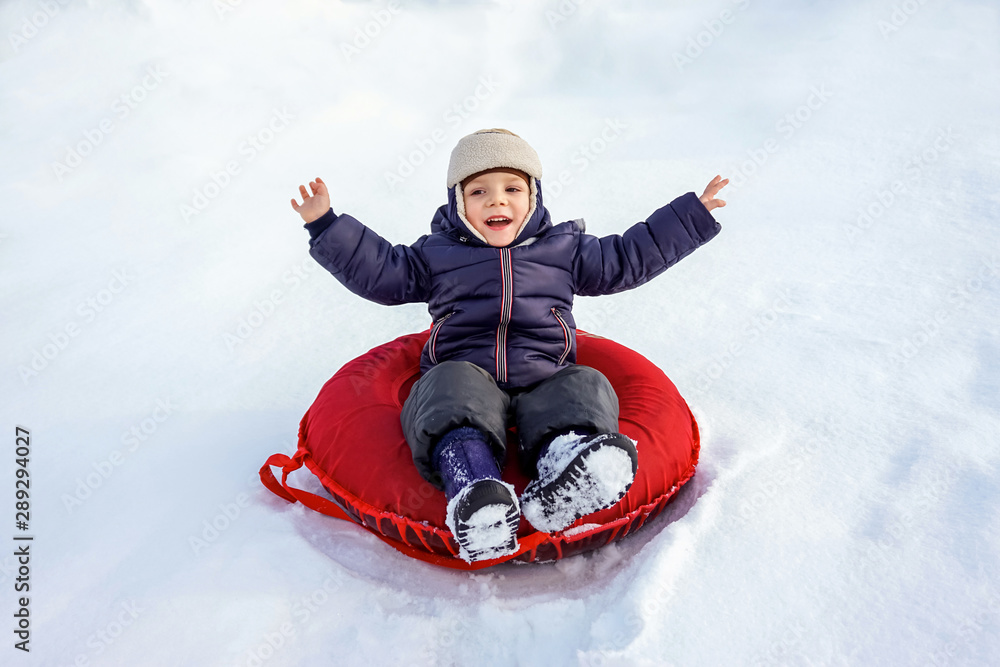happy joyful beautiful child boy rides from the mountain on a red tubing in winter happy joyful beautiful child boy rides from the mountain on a red tubing in winter