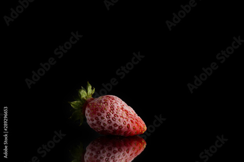one red frozen strawberry covered with hoarfrost lies on a mirror surface on a black background.
