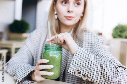Young cute blondie caucasian pretty girl drinking vegan green smoothie in summer cafe. Healthy lifestyle, beauty, youth concept