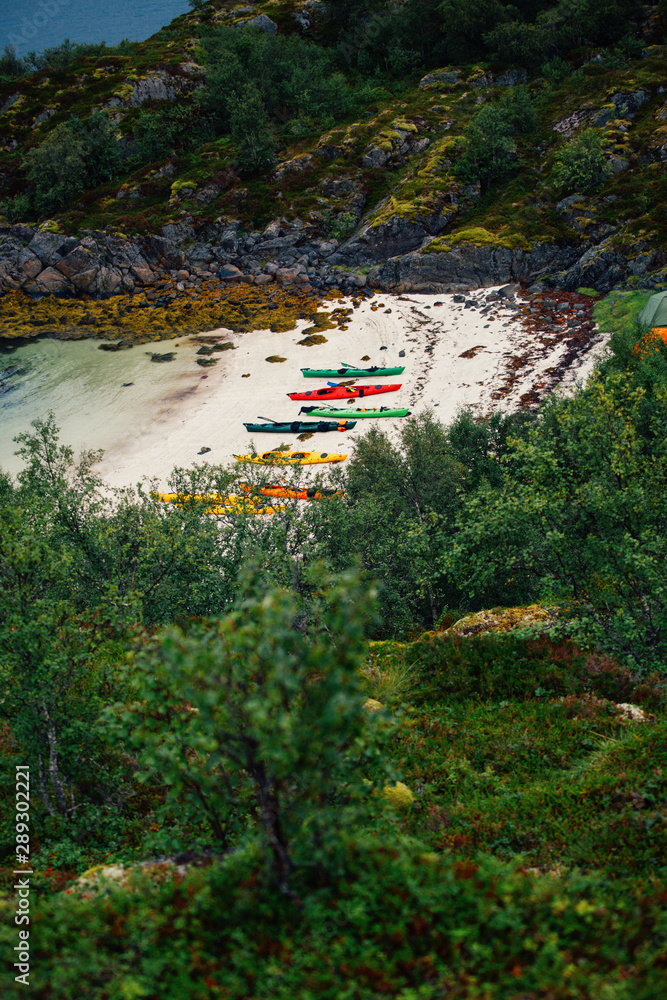 Photo of picturesque mountainous area, colorful kayaks on sandy seashore in Norway.