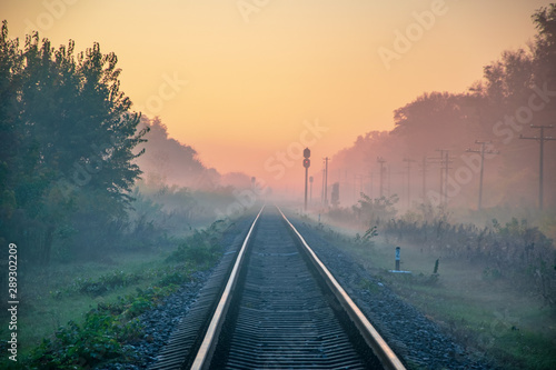 Early morning view of railway line going straight ahead through autumn fog to rising sun