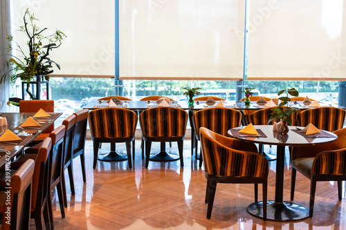 Served tables in the hotel restaurant. The banquet room is ready to receive guests. Roller blinds omitted and a Chinese plant in the corner.