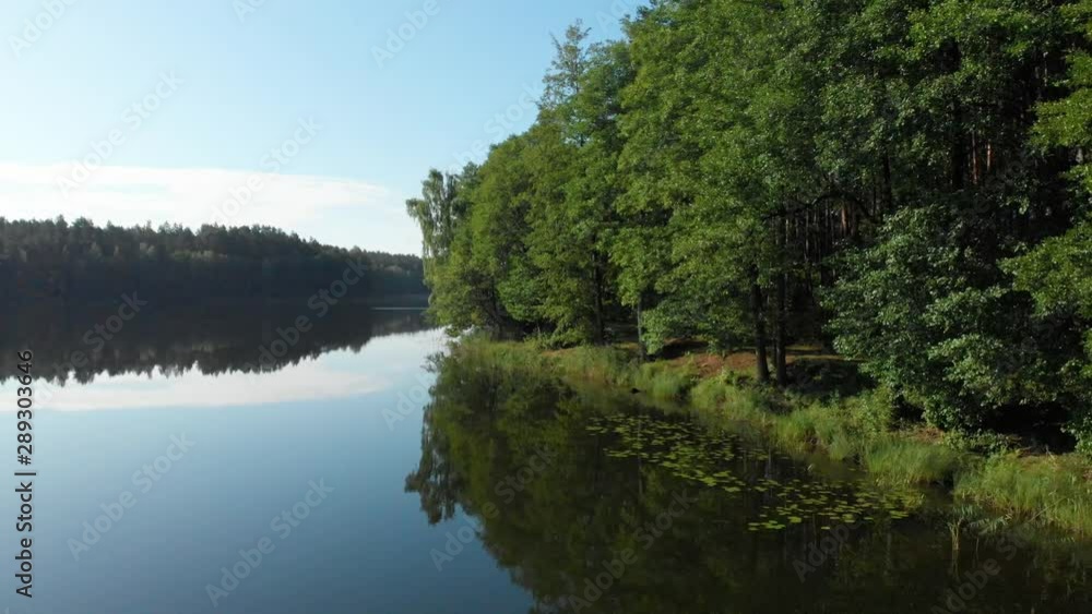 Aerial flying over a wooden pier and into the trees at the edge of a calm lake reflecting the summer sky of Lithuania Aerial flying over a wooden pier and into the trees at the edge of a calm lake reflecting the summer sky of Lithuania