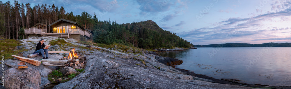 panoramic view woman reading near campfire in norway